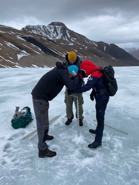 3 people stand on the glacier surface, drilling the ablation stakes